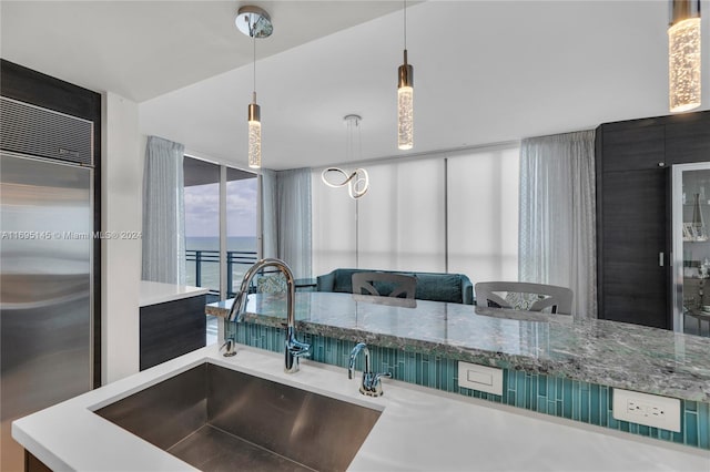 kitchen featuring stainless steel built in fridge, a water view, decorative light fixtures, and sink