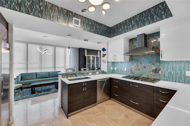 kitchen with sink, wall chimney exhaust hood, stainless steel appliances, hanging light fixtures, and white cabinets