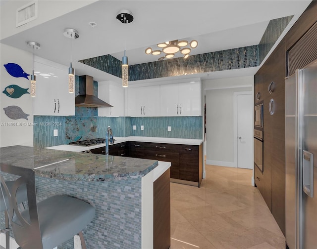 kitchen featuring wall chimney range hood, kitchen peninsula, decorative light fixtures, dark brown cabinets, and white cabinetry