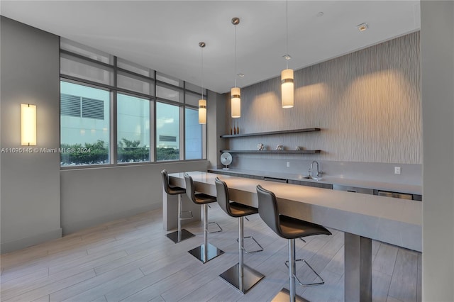 kitchen with sink, a breakfast bar, hanging light fixtures, and light hardwood / wood-style flooring