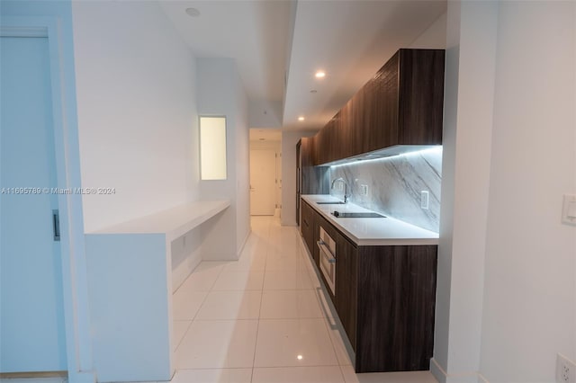 kitchen featuring black electric stovetop, backsplash, dark brown cabinetry, sink, and light tile patterned floors