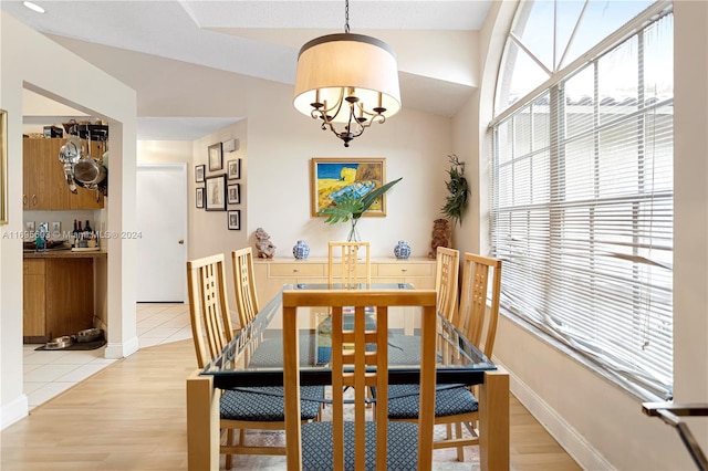 dining area with a notable chandelier, lofted ceiling, and light wood-type flooring