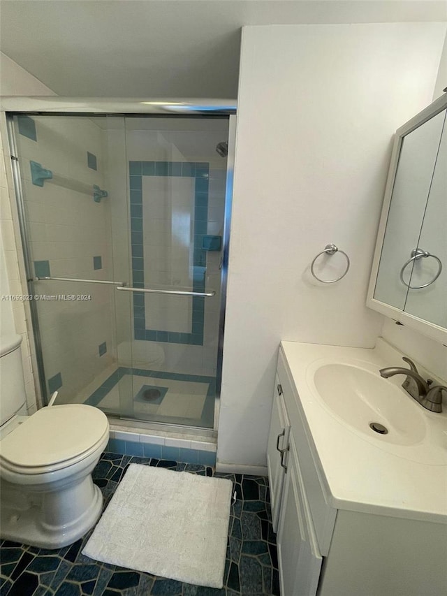 bathroom with tile patterned flooring, vanity, a shower with shower door, and toilet