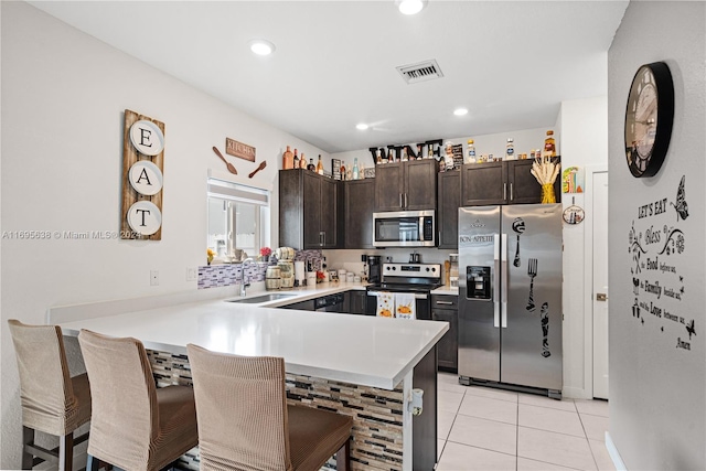 kitchen with dark brown cabinetry, sink, stainless steel appliances, kitchen peninsula, and a breakfast bar area