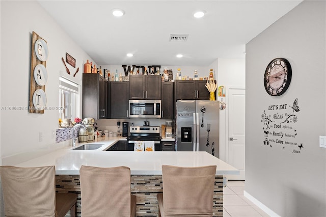 kitchen featuring a kitchen bar, appliances with stainless steel finishes, kitchen peninsula, dark brown cabinetry, and light tile patterned floors