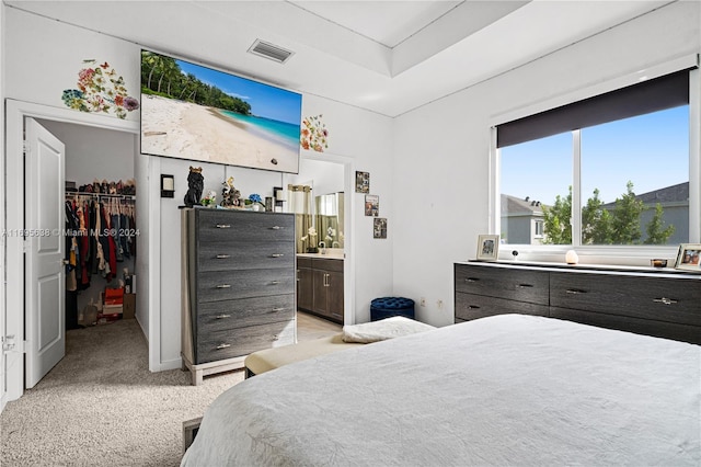 bedroom with a walk in closet, light carpet, connected bathroom, and a closet