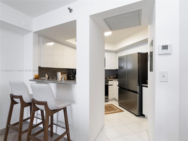 kitchen with stainless steel fridge, backsplash, a breakfast bar, light tile patterned floors, and white cabinetry