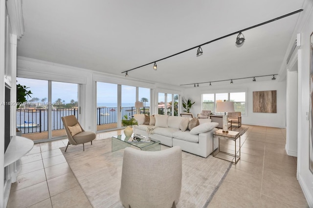 living room with rail lighting, a water view, ornamental molding, and light tile patterned flooring