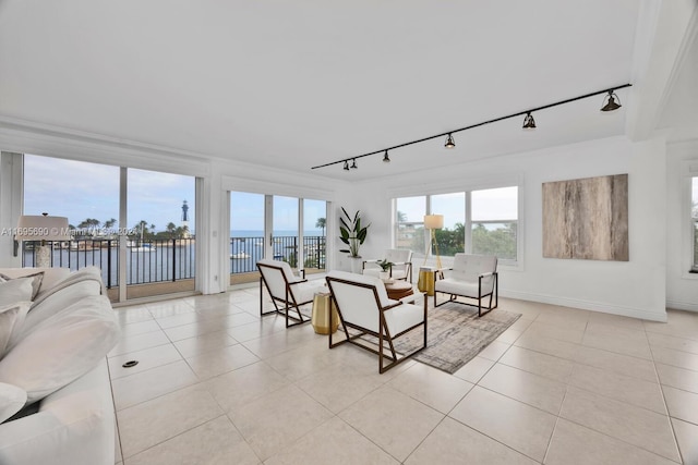 living room with a water view, light tile patterned floors, rail lighting, and ornamental molding