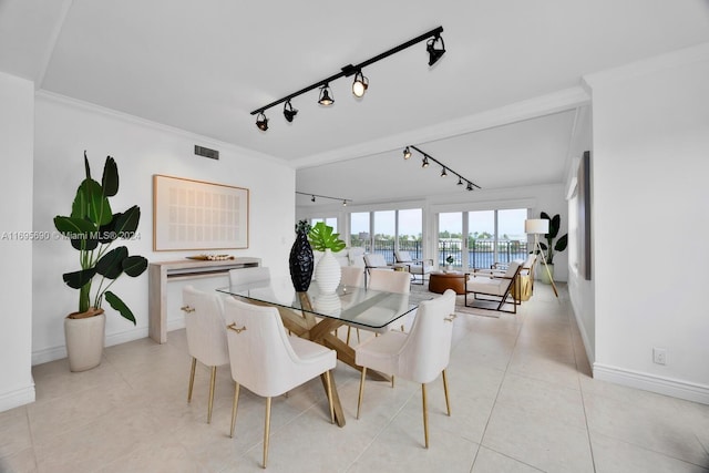 tiled dining space featuring rail lighting, a water view, and crown molding