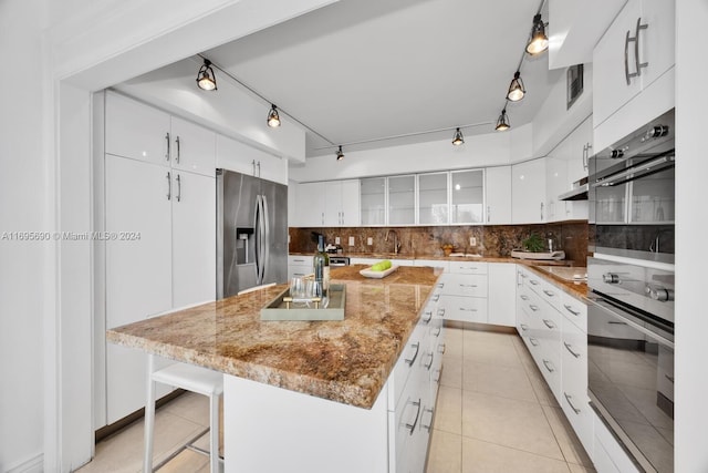 kitchen featuring stainless steel fridge, light stone counters, a kitchen island with sink, light tile patterned floors, and white cabinetry