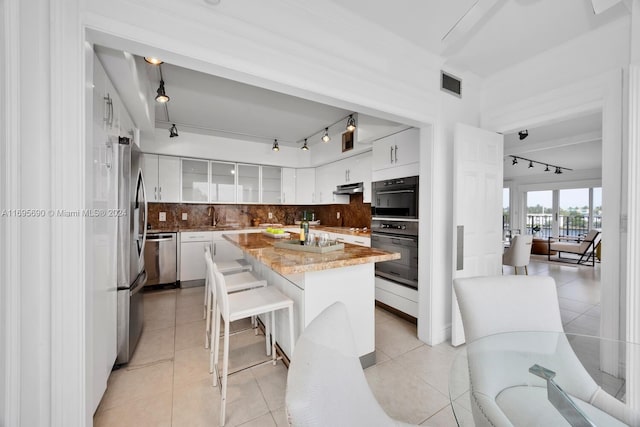 kitchen featuring rail lighting, tasteful backsplash, light tile patterned floors, white cabinets, and a kitchen island