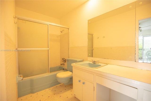 full bathroom featuring tile patterned floors, toilet, shower / bath combination with glass door, vanity, and tile walls