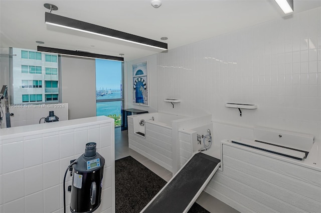 bathroom with tile patterned flooring, a bath, floor to ceiling windows, and tile walls