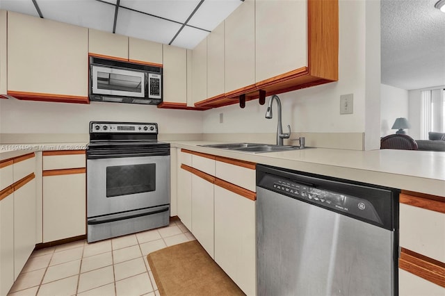 kitchen with a paneled ceiling, stainless steel appliances, sink, light tile patterned floors, and white cabinets