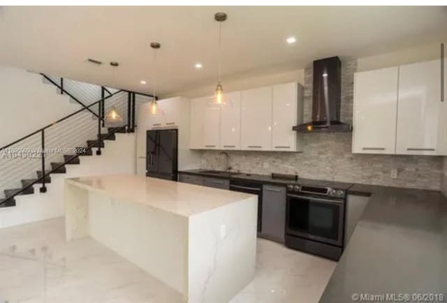 kitchen with white cabinetry, a kitchen island, decorative light fixtures, and wall chimney range hood