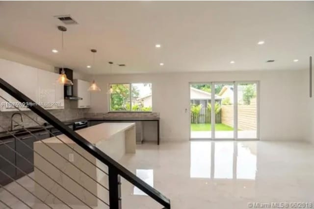 kitchen featuring plenty of natural light, white cabinetry, decorative light fixtures, and wall chimney range hood