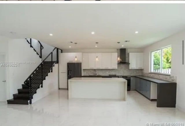 kitchen with a center island, wall chimney exhaust hood, sink, tasteful backsplash, and white cabinets