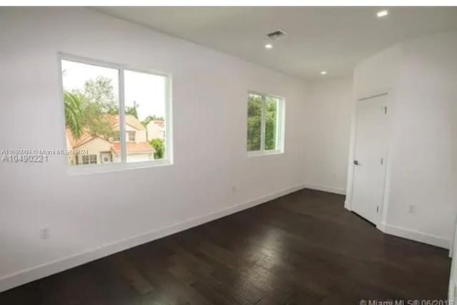 empty room with a wealth of natural light and dark hardwood / wood-style flooring