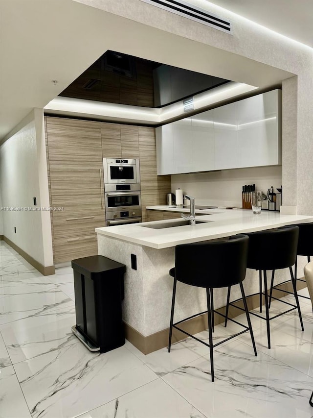 kitchen featuring sink, stainless steel double oven, a kitchen breakfast bar, kitchen peninsula, and white cabinets