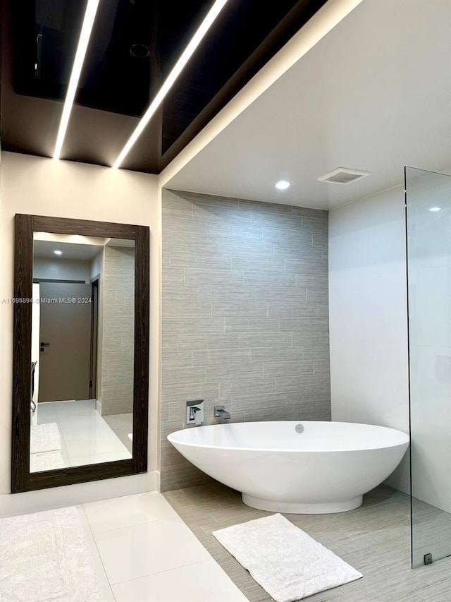 bathroom with tile patterned floors, a tub to relax in, and tile walls