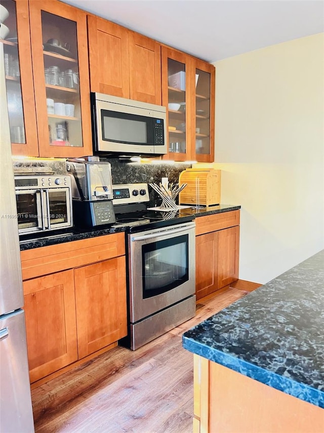 kitchen with stainless steel appliances, light hardwood / wood-style flooring, and dark stone counters