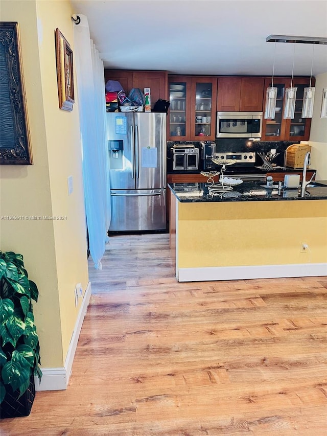 kitchen with sink, hanging light fixtures, light hardwood / wood-style flooring, dark stone counters, and appliances with stainless steel finishes