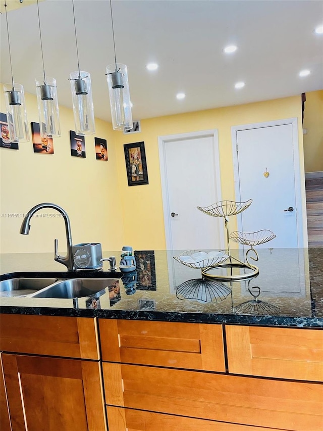 kitchen with wood-type flooring, hanging light fixtures, dark stone counters, and sink