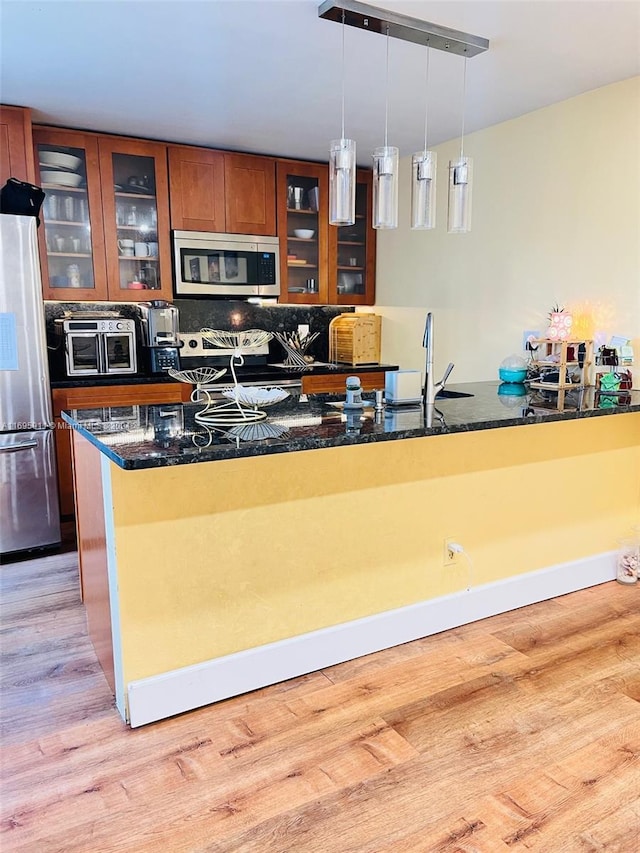 kitchen with stainless steel appliances, light hardwood / wood-style flooring, hanging light fixtures, and dark stone counters