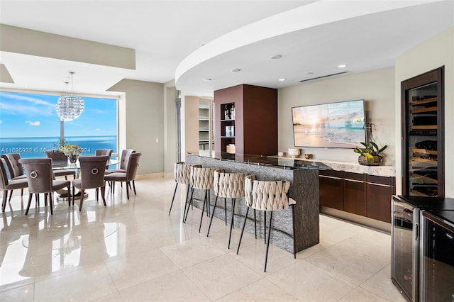 kitchen featuring dark brown cabinetry, hanging light fixtures, a notable chandelier, a breakfast bar, and a water view