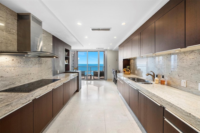 kitchen featuring backsplash, a water view, light stone counters, and wall chimney exhaust hood