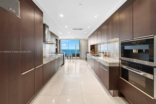 kitchen with a water view, sink, light stone countertops, light tile patterned floors, and double oven