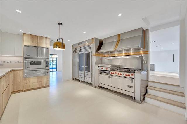 kitchen with decorative backsplash, appliances with stainless steel finishes, decorative light fixtures, and wall chimney range hood