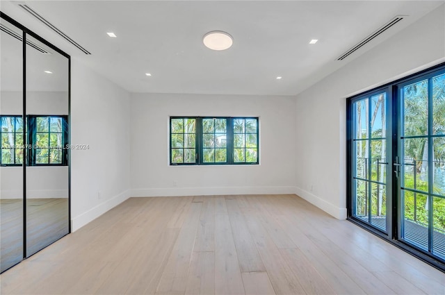 empty room with french doors, a wealth of natural light, and light hardwood / wood-style flooring