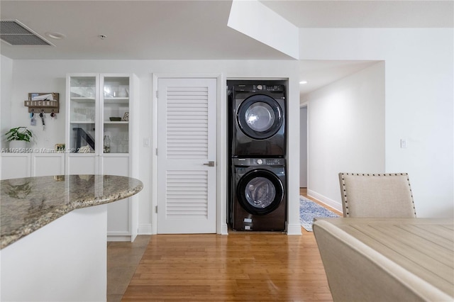 laundry area featuring stacked washer and dryer and light hardwood / wood-style flooring