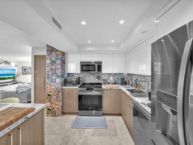 kitchen with stainless steel appliances, decorative backsplash, a tray ceiling, white cabinetry, and sink