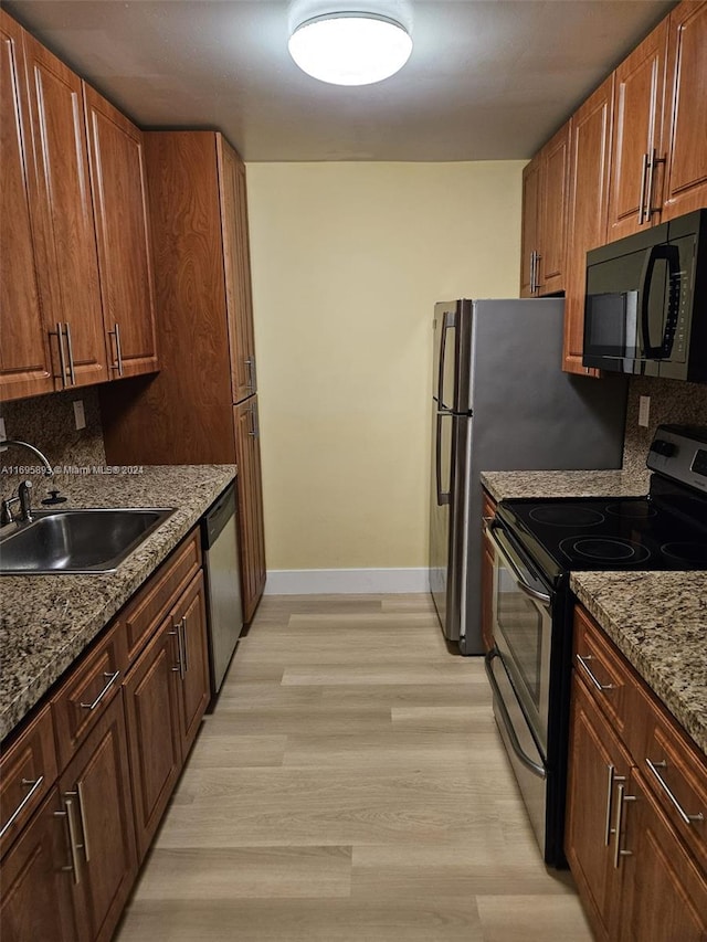 kitchen with backsplash, sink, light wood-type flooring, light stone counters, and stainless steel appliances