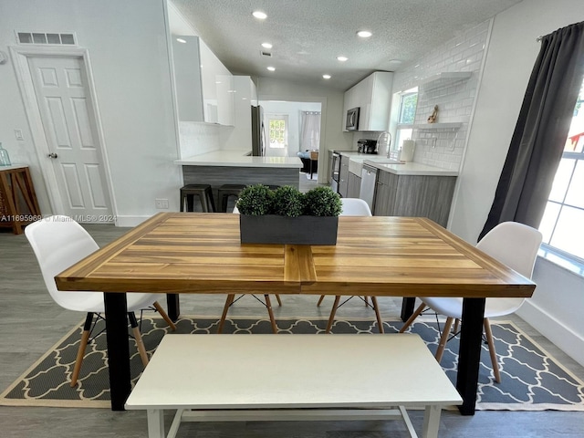 dining area with wood-type flooring, a textured ceiling, and vaulted ceiling