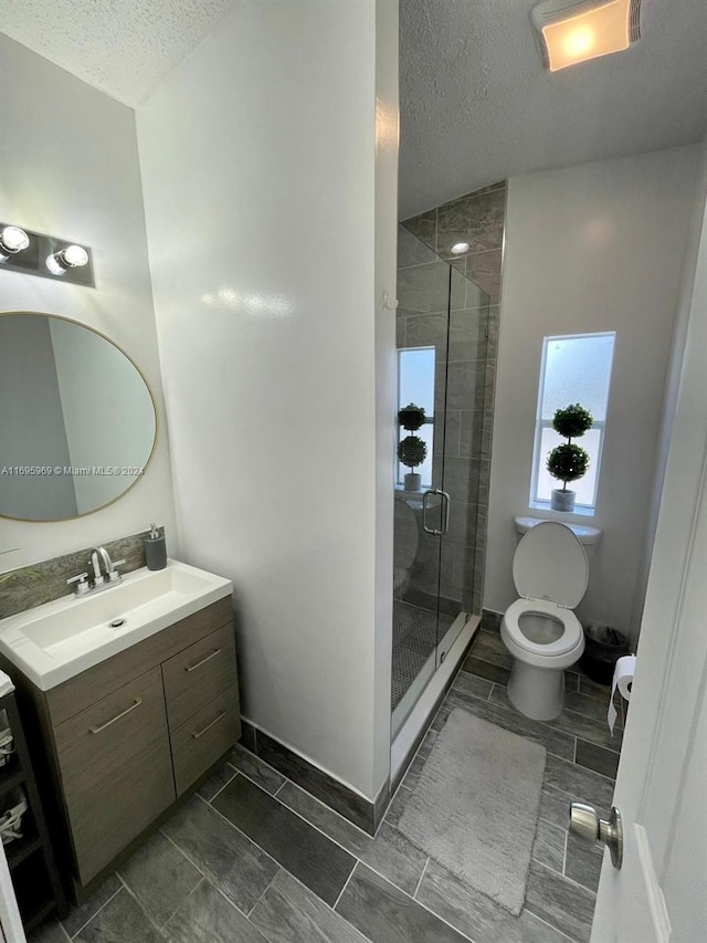 bathroom featuring vanity, toilet, a shower with door, and a textured ceiling