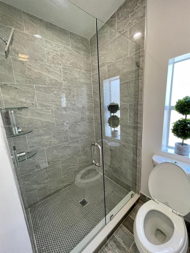 bathroom with a textured ceiling, toilet, and a shower with shower door