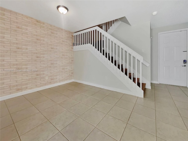 staircase with tile patterned floors and brick wall