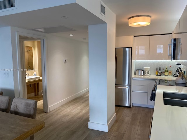 kitchen with appliances with stainless steel finishes, backsplash, light hardwood / wood-style floors, and white cabinetry