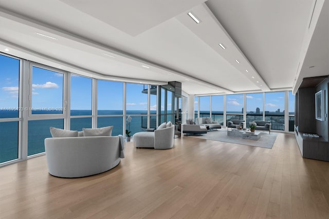 living room with floor to ceiling windows, a water view, and light wood-type flooring