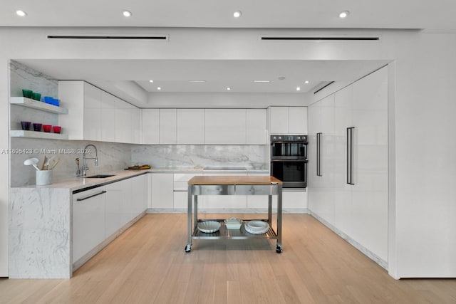 kitchen with dishwashing machine, light wood-type flooring, white cabinetry, and backsplash