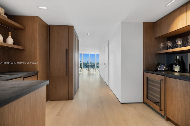 corridor with expansive windows, beverage cooler, and light hardwood / wood-style flooring