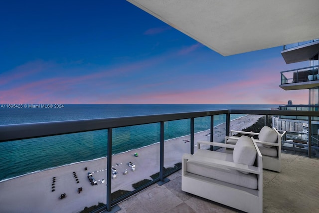 balcony at dusk featuring a water view and a view of the beach