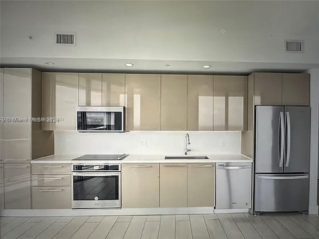 kitchen featuring cream cabinets, sink, stainless steel appliances, and light hardwood / wood-style flooring