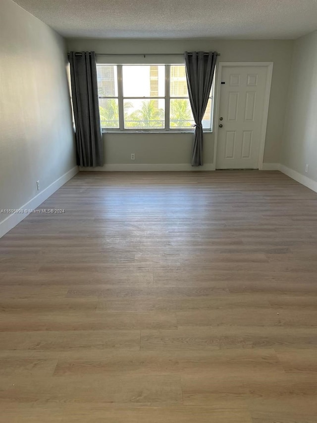 401 Golden Isles Dr Unit 303, Hallandale Beach, FL 33009 - unfurnished room with light wood-style flooring, baseboards, and a textured ceiling