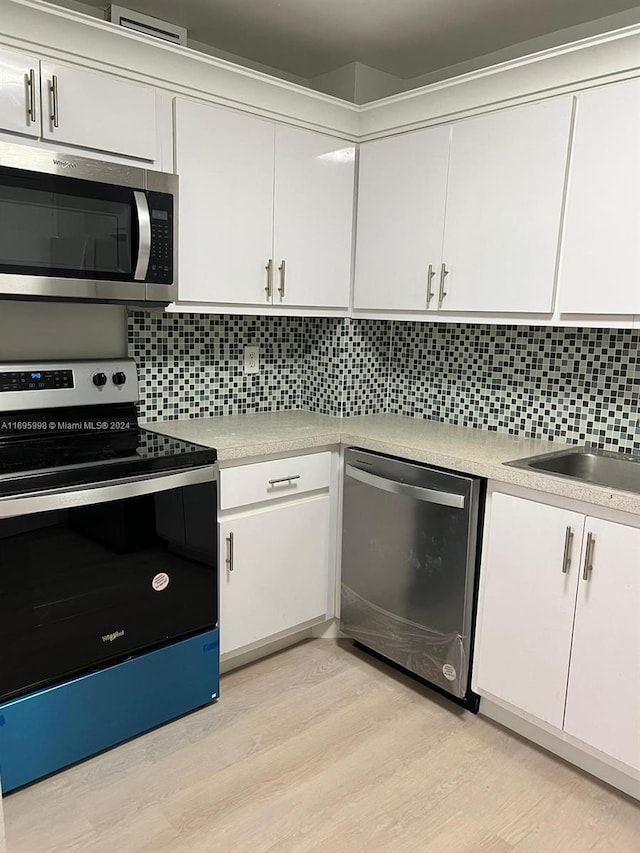 kitchen featuring white cabinets, backsplash, appliances with stainless steel finishes, and light hardwood / wood-style flooring