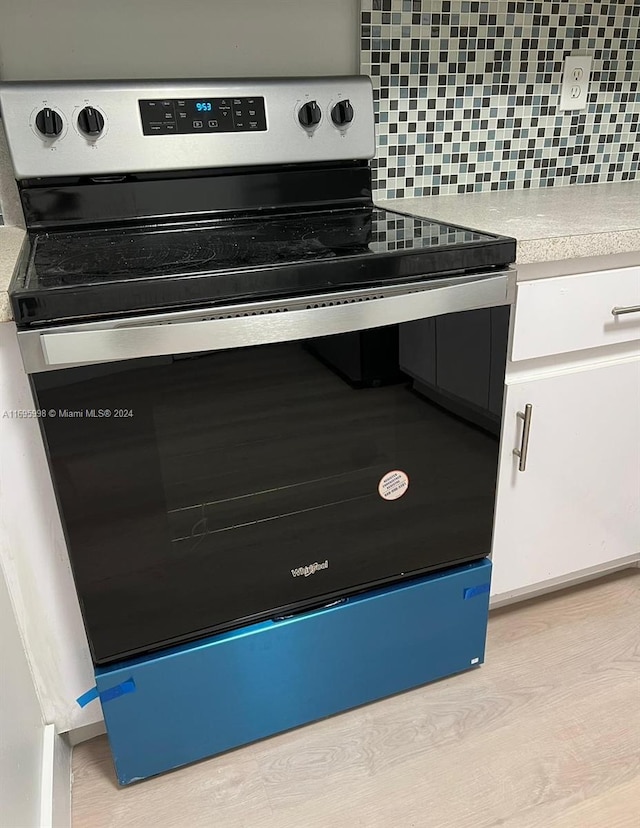 interior space featuring tasteful backsplash, white cabinets, stainless steel range with electric cooktop, and light wood-type flooring